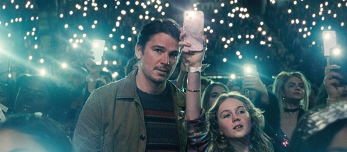 Josh Hartnett and Ariel Donoghue at a music concert, the lights on their phone lighting up the dark.