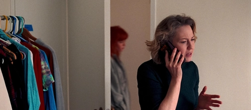 Carrie Coon speaks on the phone as Natasha Lyonne walks by in the background of 2024 Netflix film 'His Three Daughters'.